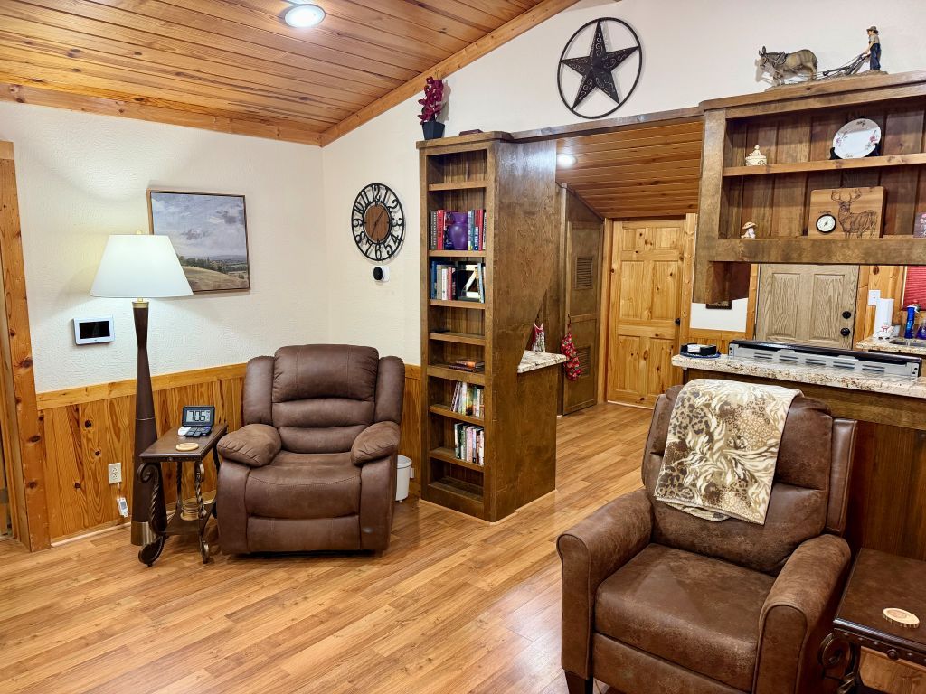 A room with a wooden ceiling, a fireplace, a bookshelf, a clock, and a dining area.