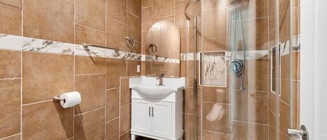 A bathroom with a glass-enclosed shower, a white sink, and a marble-tiled wall.