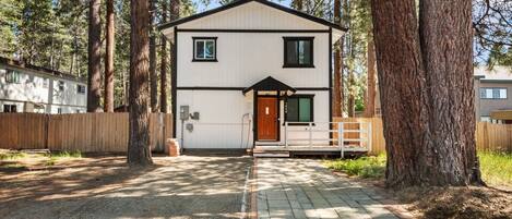 A two-story building with a white exterior and black trim, surrounded by tall trees.