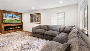 A living room with a flat-screen TV, fireplace, grey sofa, patterned rug, and a framed picture on the wall. - Walk to Lake Tahoe | Sleeps 10 | EV Charger (South Lake Tahoe)