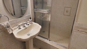 Een badkamer met een wastafel, spiegel, douche en een handdoek met een palmprentenmotief.