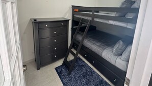 Een slaapkamer met een stapelbed, een dressoir en een tv die aan de muur hangt.