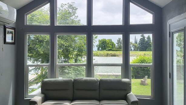 A room with a large window, a ceiling fan, and a beige sofa.