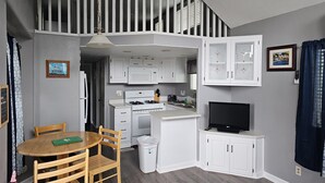 A compact kitchen with white cabinets, a stove, and a TV.