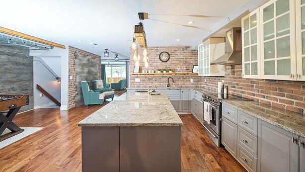 A modern kitchen with a central island, grey cabinetry, and a brick accent wall.