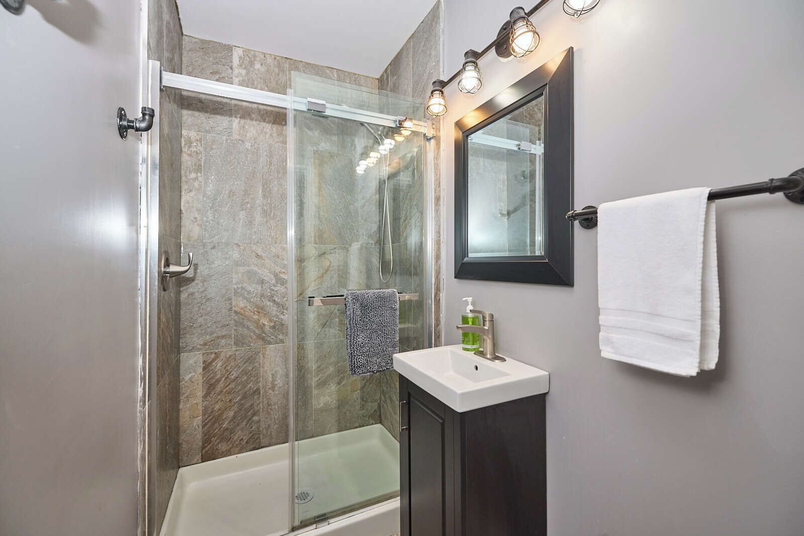 A modern bathroom with a glass-enclosed shower, a white sink, and a mirror with lights above.