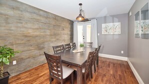 A dining room with a wooden table, chairs, a hanging light fixture, and a potted plant.