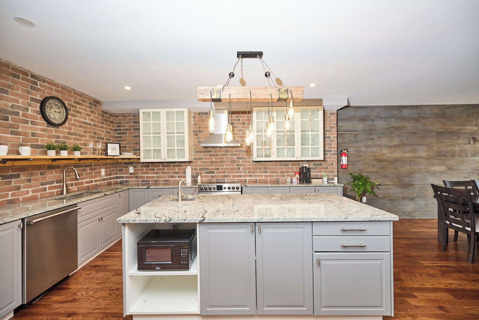 Een keuken met een centraal eiland, een bakstenen muur en een hangende lamp.
