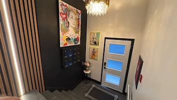 A hallway with a black wall, a wooden slat wall, a door with three windows, and a chandelier.