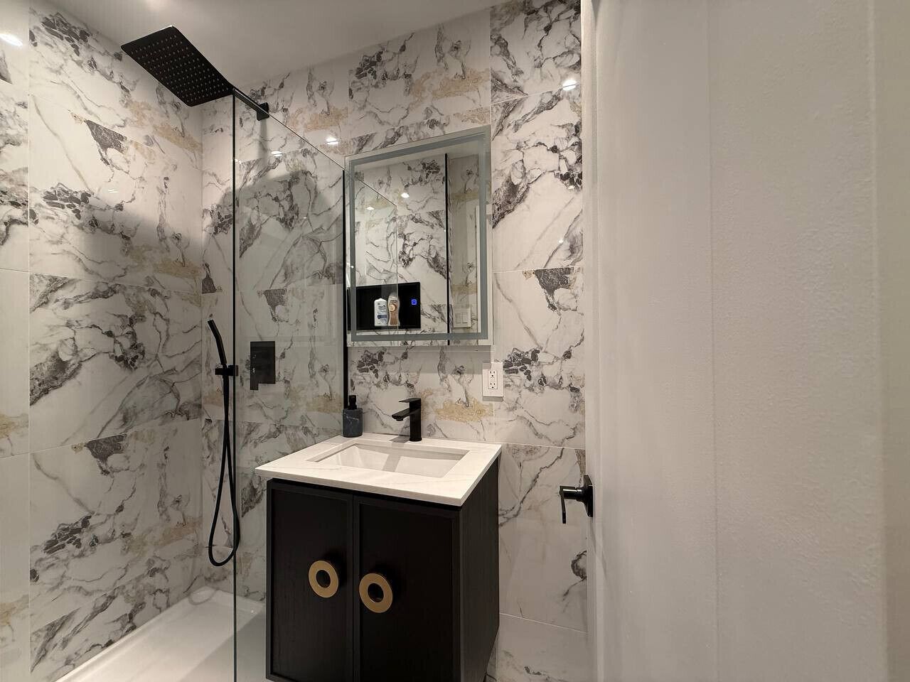 Ein modernes Badezimmer mit einer gläsernen Duschkabine, einem weißen Waschbecken und einer Wand mit Marmoroptik.
