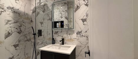 Une salle de bain moderne avec une douche à parois de verre, un lavabo blanc et un mur décoré d’un motif marbré.