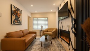 A living room with a sofa, armchair, coffee table, fireplace, and abstract art on the wall.