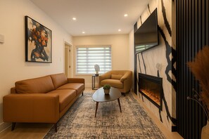 Una sala de estar con sofá, sillón, mesa de centro, chimenea y arte abstracto en la pared.
