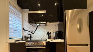 A modern kitchen with a built-in oven, a stainless steel refrigerator, and a window with blinds.