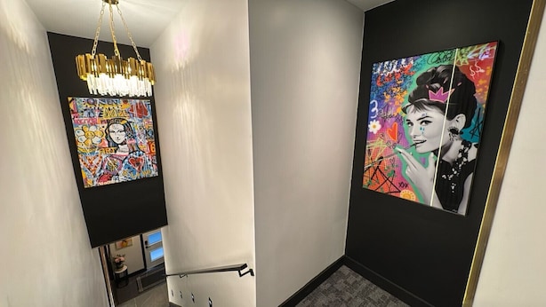 A hallway with a modern chandelier, a colorful abstract painting, and a framed portrait on the wall.