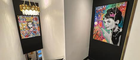 A hallway with a modern chandelier, a colorful abstract painting, and a framed portrait on the wall.