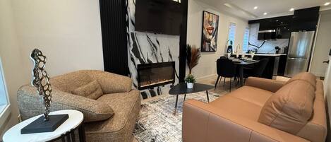 A modern living room with a fireplace, sofa, coffee table, and dining area.