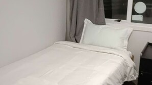 A single bed with white bedding, a grey curtain, and a window with a white frame. - 2 Bedroom Garden Chalet (Rotorua)
