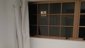 A single bed with a white mattress and a folded white blanket in a room with a window and curtains. - 2 Bedroom Garden Chalet (Rotorua)