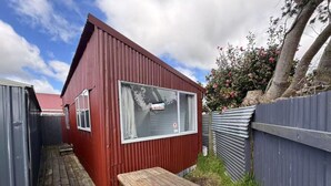 A small red building with a window and a wooden bench in front. - 2 Bedroom Garden Chalet (Rotorua)