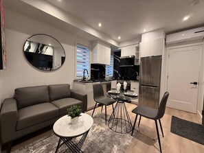 A modern living room with a sofa, a round coffee table, and a dining area with chairs. - Le Style & Fashion 1BR Downtown Atwater Nightlife (Montréal)