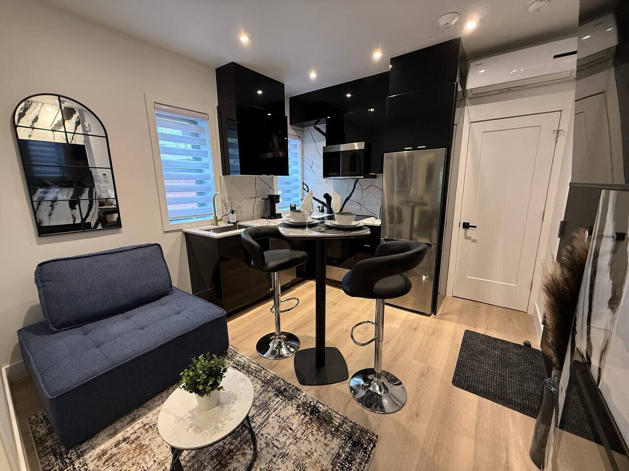 A modern kitchen with black cabinets, a stainless steel refrigerator, and a dining area with a round table and bar stools.