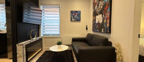 A modern living room with a fireplace, a black leather sofa, a round coffee table, and a large painting on the wall.