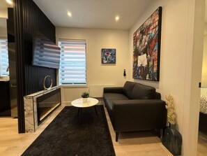 Ein modernes Wohnzimmer mit Kamin, einem schwarzen Ledersofa, einem runden Couchtisch und einem großen Gemälde an der Wand.