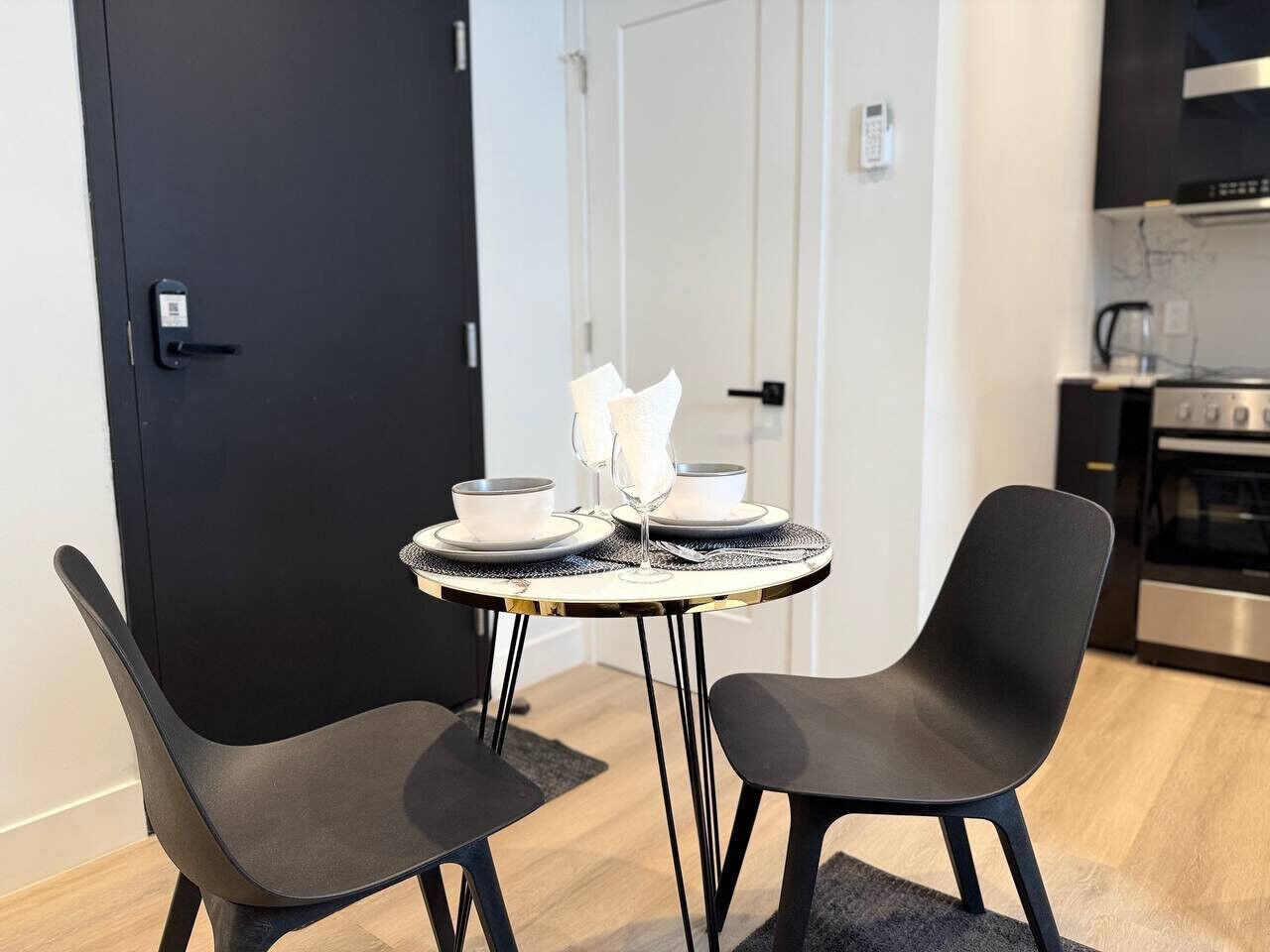 A modern kitchen with a black door, a dining table with two chairs, and a small island with a white countertop.