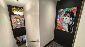 Ein Flur mit einem modernen Kronleuchter, einem farbenfrohen abstrakten Gemälde und einem gerahmten Porträt an der Wand.