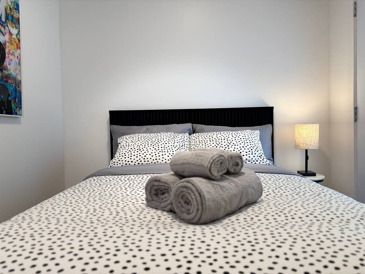 Una cama bien hecha con toallas enrolladas, una colcha estampada y una lámpara de noche.