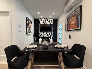 Un coin repas avec une table sombre dressée pour deux personnes, un vase décoratif et des œuvres d’art accrochées aux murs.