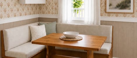 Una habitación de esquina con una mesa de madera, un banco y una ventana con cortinas.