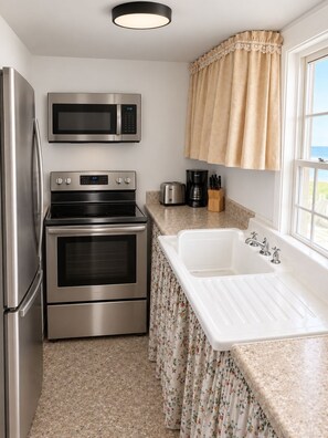 A kitchen with stainless steel appliances, a white sink, and a window with curtains. - Oceanview Cottage - Beach - Peaceful - Amazing Views (Malpeque)