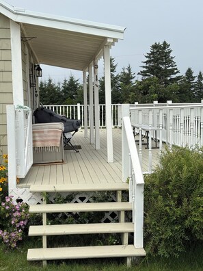 A covered outdoor deck with a grill, seating, and a railing. - Oceanview Cottage - Beach - Peaceful - Amazing Views (Malpeque)
