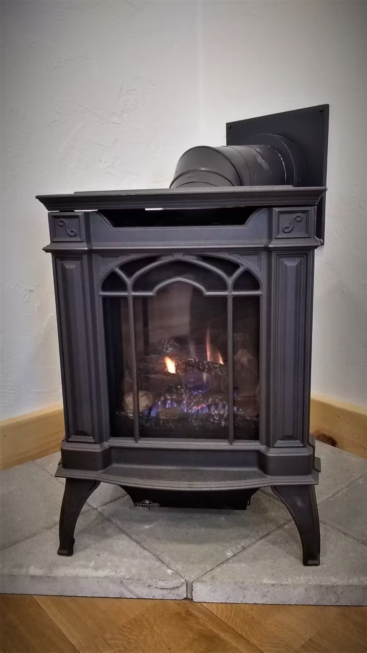 A black wood-burning stove with a glass door, set on a concrete floor against a plain wall.