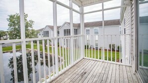 A covered porch with a view of a residential area, including houses and a body of water. - 2-bedroom condo in tranquil Surfside with cool AC breeze (Surfside)