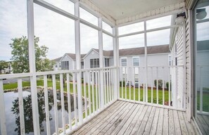 A covered porch with a view of a residential area, including houses and a body of water. - 2-bedroom condo in tranquil Surfside with cool AC breeze (Surfside)