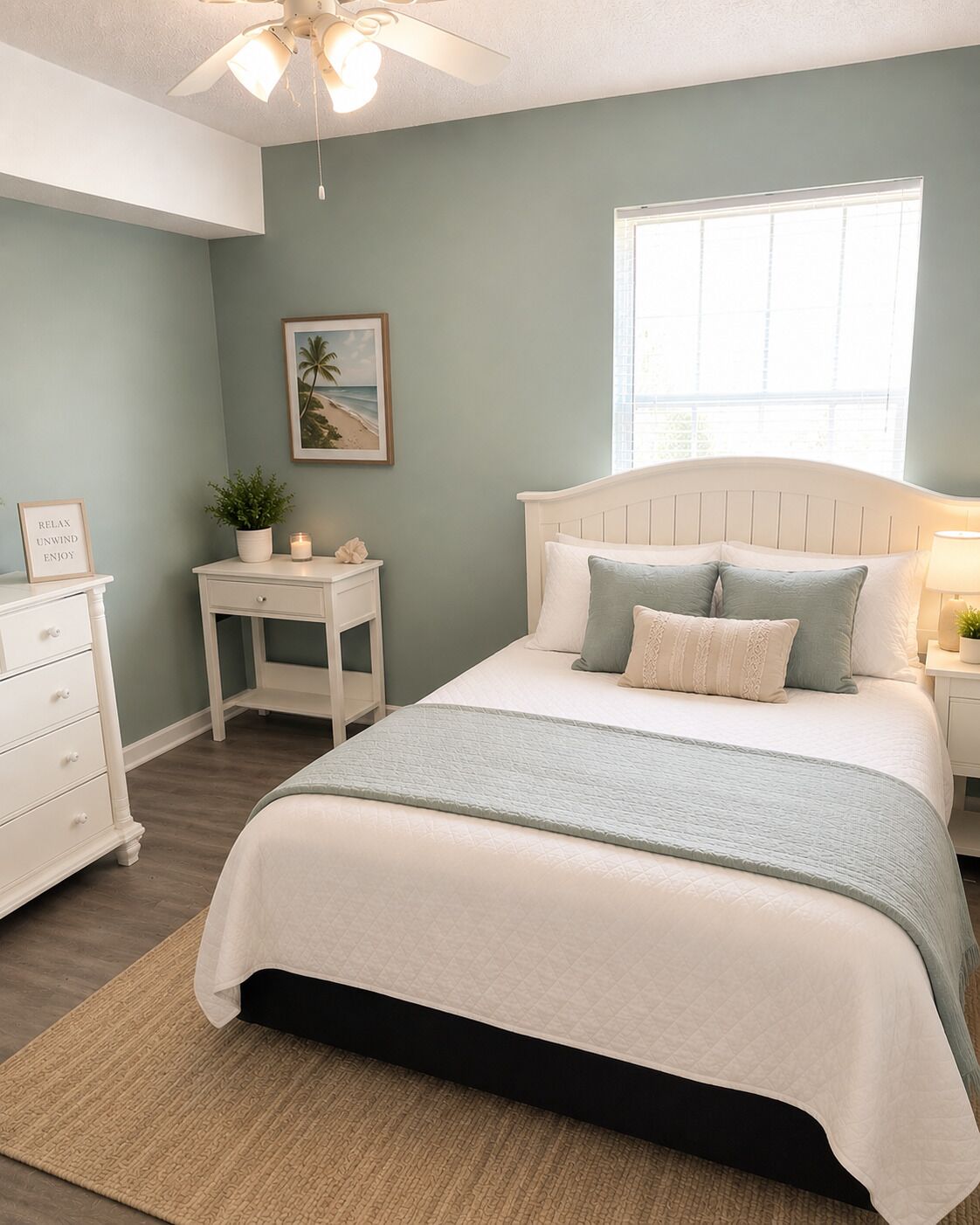 Une chambre à coucher comprenant un lit, des tables de chevet, une commode, un ventilateur de plafond, une fenêtre et un tableau encadré accroché au mur.