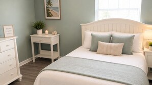 A bedroom with a bed, nightstands, a dresser, a ceiling fan, a window, and a framed picture on the wall. - 2-bedroom condo in tranquil Surfside with cool AC breeze (Surfside)