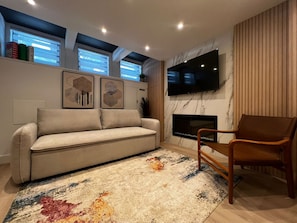 A living room with a sofa, a chair, a flat-screen TV, a fireplace, and artwork on the wall. - Le Urban Cool! NEW Stylish Crash Pad Central MTL (Montréal)