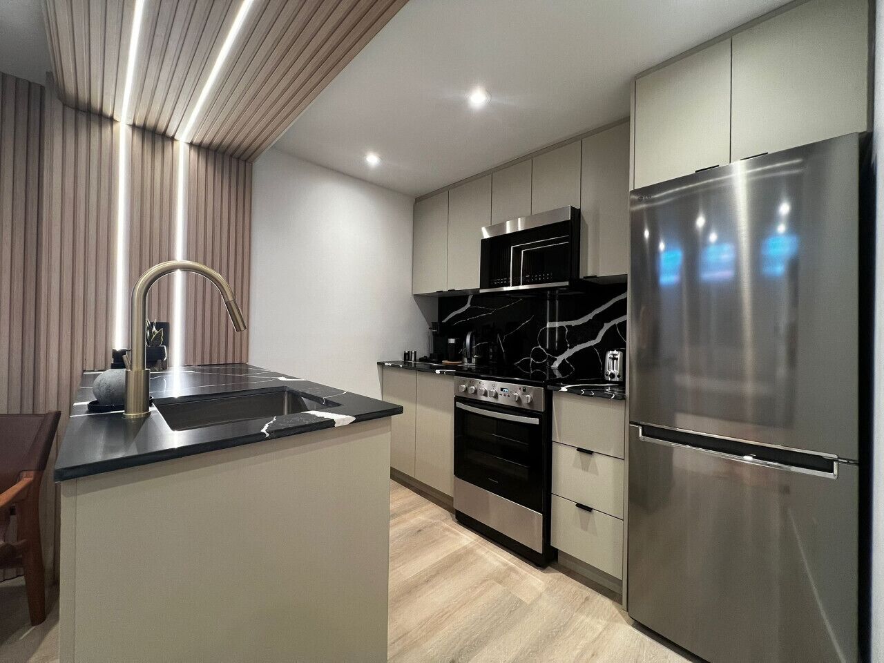 A modern kitchen with a central island, stainless steel appliances, and a wooden ceiling.