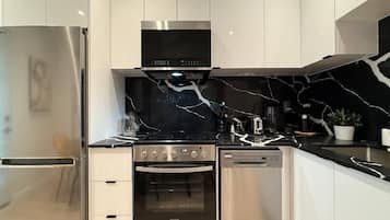 Een moderne keuken met roestvrijstalen apparatuur, een zwarte marmeren achterwand en witte kastjes.