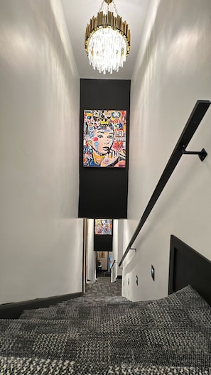 Ein Flur mit einer Chandelüster, einem großen abstrakten Gemälde und einer Treppe.