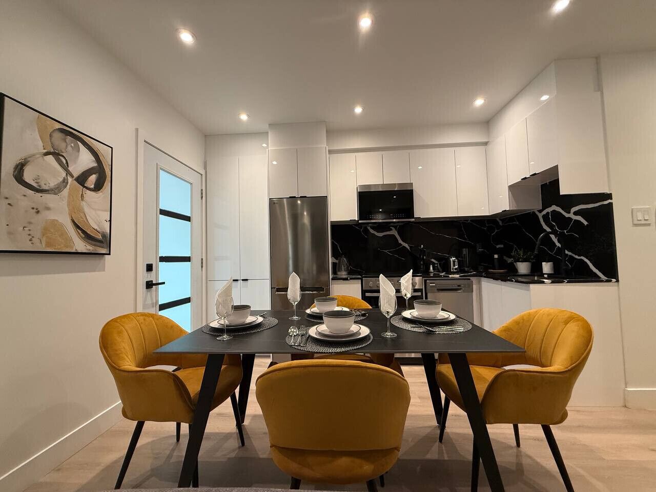 Een moderne eetruimte met een zwarte tafel, gele stoelen en een zwart-wit marmeren achterwand.