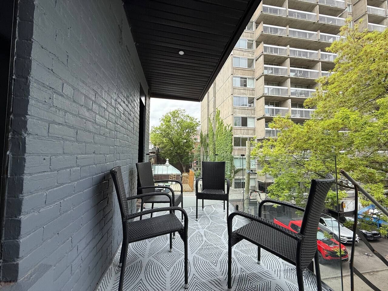 Un área de estar al aire libre cubierta con sillas y una mesa, un muro de ladrillo y vistas a un edificio de varios pisos.