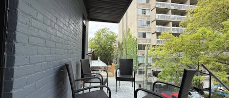 Un área de estar al aire libre cubierta con sillas y una mesa, un muro de ladrillo y vistas a un edificio de varios pisos.