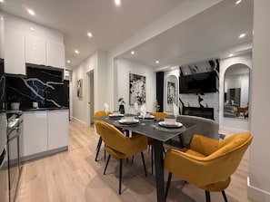 Un espace repas moderne avec une table noire, des chaises jaunes et une cuisine dotée de meubles blancs et d’un plan de travail noir.