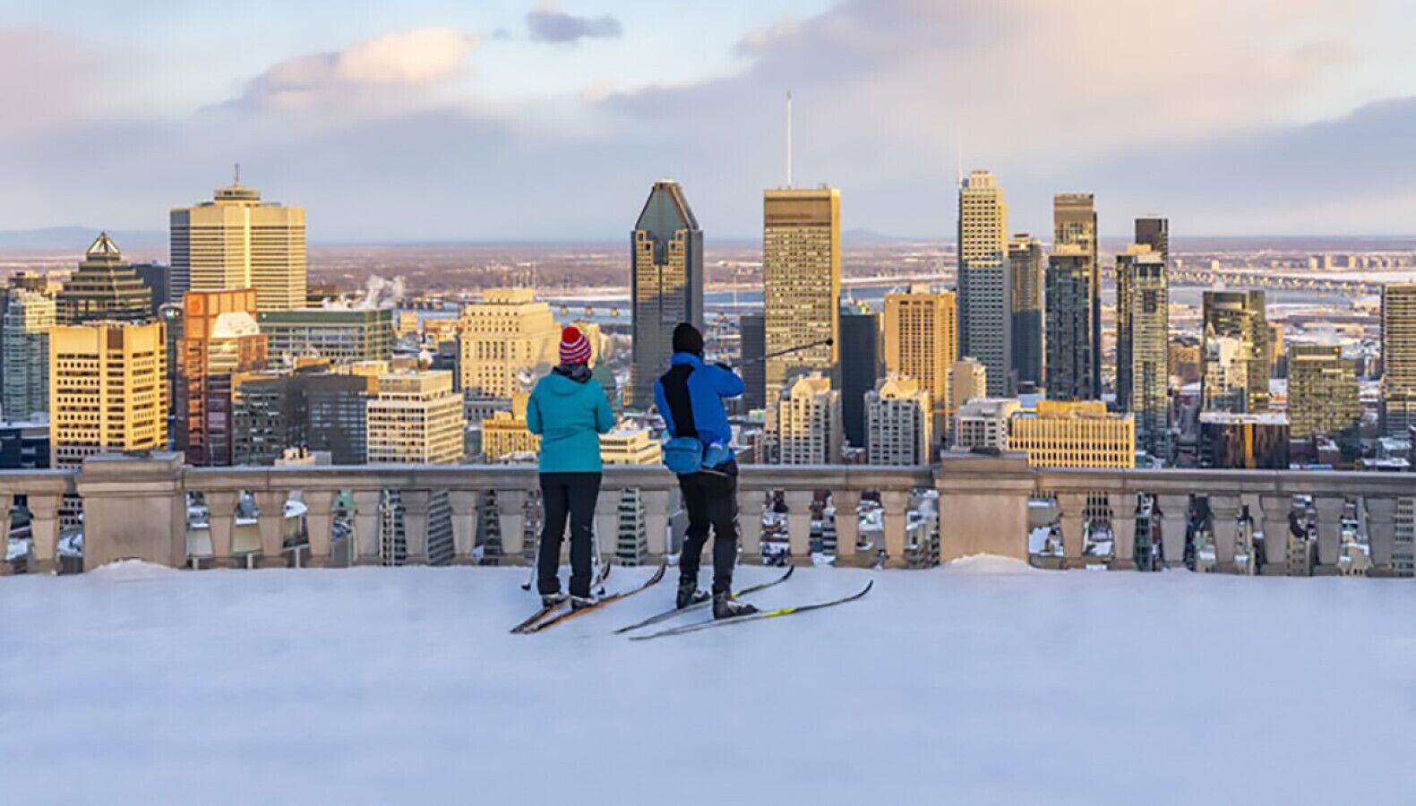 Two people skiing on a snowy slope with a cityscape in the background.