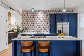 A modern kitchen with a central island, blue cabinets, and patterned wallpaper.